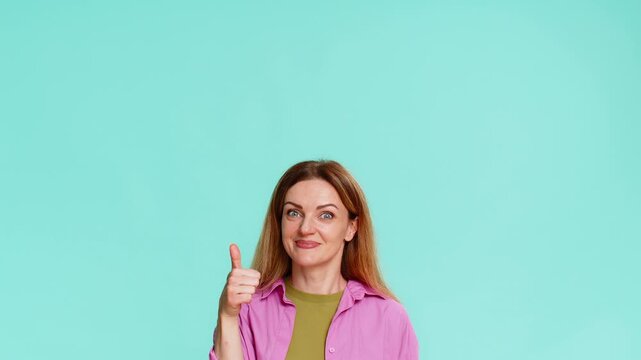 Middle-aged woman points finger upward with serious face, clearly signaling importance, asking to focus attention on something above. Girl isolated on blue background shows emphasis gesture and intent