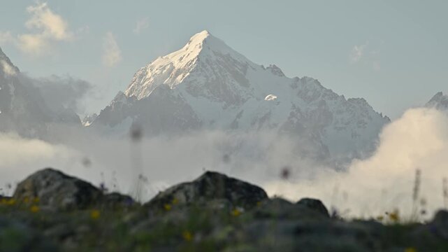 Parallax in sliding. Snow-capped mountain peak rises above clouds with rocky foreground in focus
