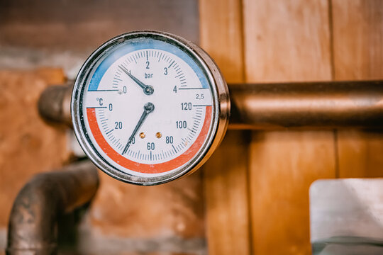 Pressure gauge on copper piping showing temperature in Celsius and pressure in bar units, part of a heating system
