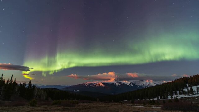 Spectacular Aurora Borealis dancing in the night sky over a mountain range with people watching.