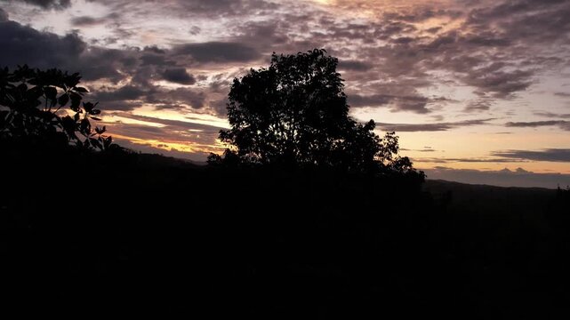 Crane drone shot reveals a golden sunset sky over the Suku Anak Dalam region in Merangin, Jambi. The bright yellow light creates a sharp silhouette against the dense tropical forest canopy. 
