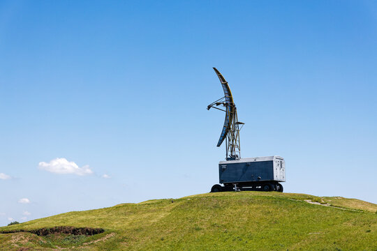 Military Radar Station on Top of a Green Hill, with its Antenna Pointed Skyward Against Clear Blue Sky