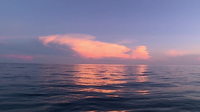 Wide shot captures the calm, rolling waves of the Central Java sea under a vivid sky. Thick clouds absorb the sunlight to turn deep orange, creating a striking vista between water and horizon. 
