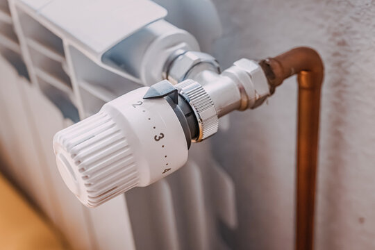 Detailed close-up of a thermostatic radiator valve with copper pipe and chrome fittings, home heating system. Energy saving concept.