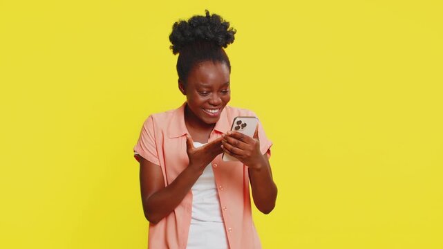 Happy excited African Black woman girl use smartphone typing browsing shouting say wow yes found out great big win good news lottery goal achievement celebrating success, winning play game on yellow