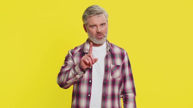 Caucasian, mature man expressing refusal by waving finger and shaking head in strong disapproval. Middle-aged guy isolated on yellow background, showing negative body language with strong no gesture
