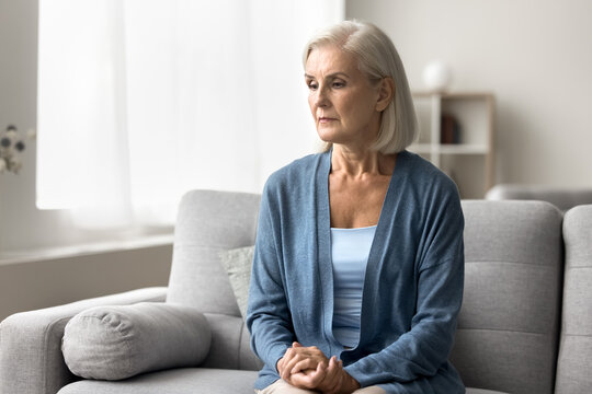 Unhappy anxious older age female sit on couch feel bad unwell check heart rate on wrist. Sad stressed elder woman feel hypertension symptoms depression troubled with climax menopause health changes