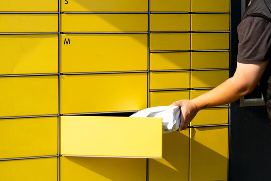 Person retrieving package from yellow delivery locker with multiple compartments in urban setting