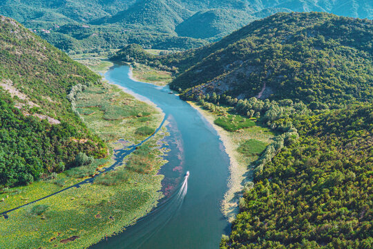 Boat creating wake while cruising along a calm river surrounded by lush green hills, mountains, and water lilies