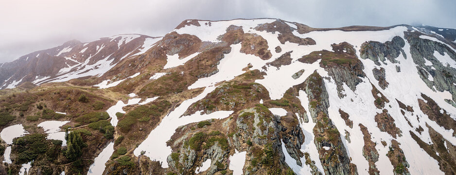 Mountain ranges showing melting snow patches on rocky terrain and greening slopes, signaling the changing seasons and nature