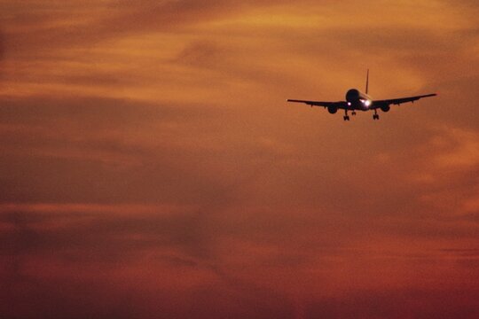 Commercial Airplane Landing at Sunset Against Orange Sky