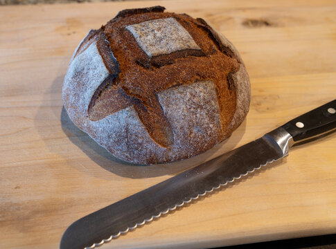 sourdough bread loaf on a wooden board with a cutting knife