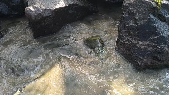 Rough coastal waves crashing onto rocky shore covered with green algae and sea foam. Murky water, sandy beach texture, and scenic horizon under a cloudy sky. Environmental nature background.