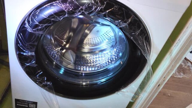 Hand removing protective plastic film from new washing machine during unboxing and initial setup.