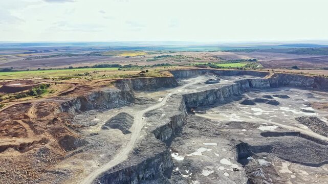 This granite quarry shows deep rock pits and machinery working in a rural area. Surrounding fields and hills are visible under a clear sky.