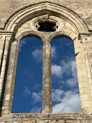 Naklejka premium Gothic stone window frame against blue sky with clouds, La Flotte, Nouvelle-Aquitaine, France, July 2025