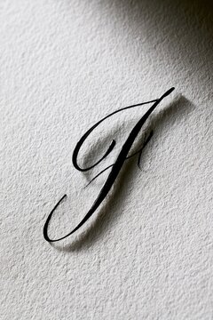 Close-up photograph of an elegant black cursive J hand-lettered on white textured paper