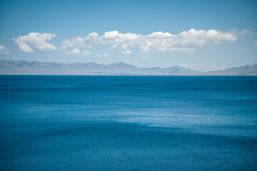 Fototapeta premium Aerial View of Sayram Lake: Pure Blue Water, Sunny Sky with Clouds and Distant Tianshan Mountains in Xinjiang
