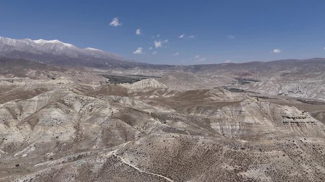 Wide drone aerial of barren hills and rugged terrain in Upper Mustang, Nepal. Scenic Himalayan desert landscape showcasing the region's remote beauty for travel and documentary projects.