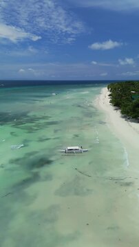 Vertical drone orbits a boat arriving at Dumaluan Beach, showing white sand, shallow turquoise water, and Panglao coastline