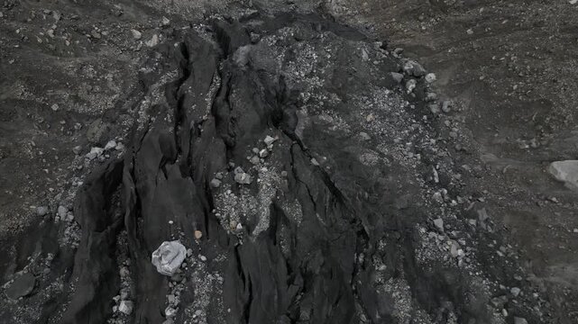 Close-up drone tracking shot over the dark, fractured rock formations and moraine debris of Karimabad Glacier Valley in Pakistan.