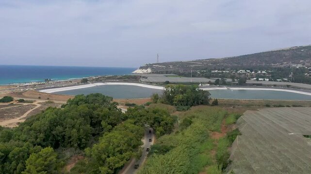 Aerial drone view of UTVs and ATVs driving on a coastal road near a water reservoir and the sea.
