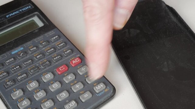 Male finger pressing buttons on scientific calculator keypad on desk with cover removed.