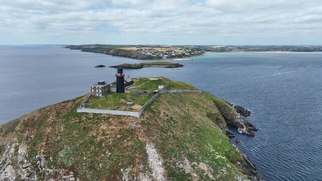 Landscape view of stunning Bally Cotton Lighthouse on the South coast of Ireland at County Cork, with a small Island between it and picturesque Ballycotton fishing village