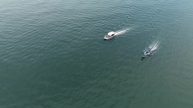 High-angle drone shot shows two motorboats crossing a vast blue sea in West Java. Small vessels navigate calm waters toward a fishing spot during a peaceful day in Sumedang. 