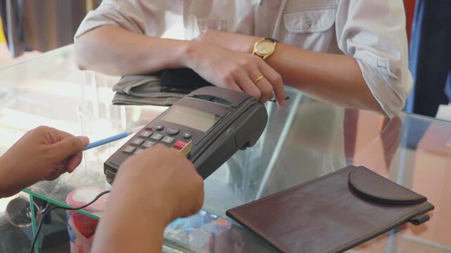 Saleswoman swiping credit card through credit card reader terminal inside fashion boutique for consumer retail shopping payment in 4K Ultra HD footage
