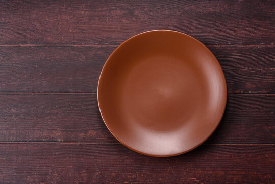 An empty round ceramic plate on a dark, textured brown background. An empty round plate