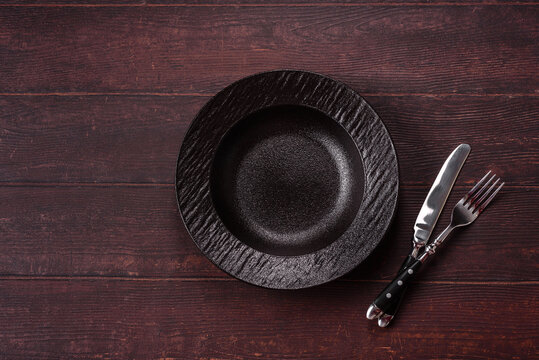 An empty round ceramic plate on a dark, textured brown background. An empty round plate