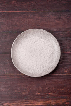 An empty round ceramic plate on a dark, textured brown background. An empty round plate