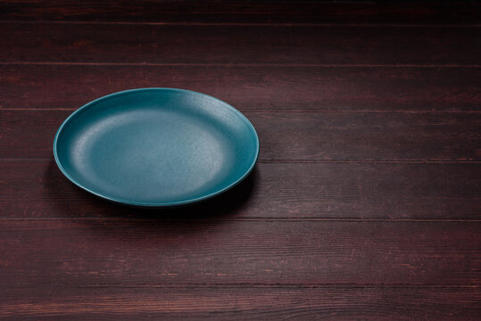 An empty round ceramic plate on a dark, textured brown background. An empty round plate