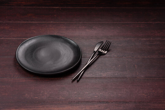 An empty round ceramic plate on a dark, textured brown background. An empty round plate