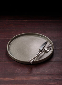 An empty round ceramic plate on a dark, textured brown background. An empty round plate