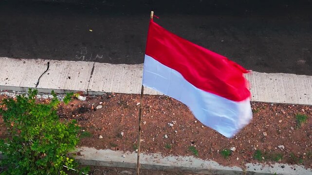 The red and white Indonesian flag flutters in the wind, attached to a bamboo pole; slow motion.