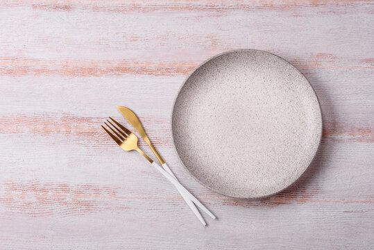 An empty round ceramic plate on a dark, textured white background. An empty round plate