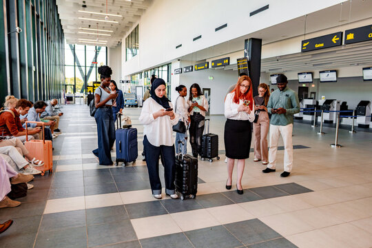 Diverse people traveling, waiting in airport terminal, using smartphones