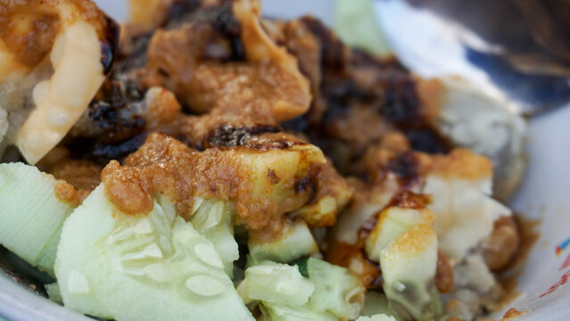 Detailed macro view showing crunchy sliced cucumber alongside batagor dumplings covered in savory peanut sauce.