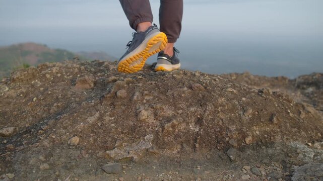 Close-up of a male trail runner's shoes climbing a rocky hillside in the afternoon, capturing determination, endurance, outdoor fitness, and adventure in nature.