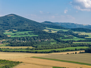 Obraz premium Aerial drone view of Biskupia Kopa mountain in the Opawskie Mountains, Poland, during summer, showing surrounding agricultural fields, forests and picturesque countryside landscape of Sudetes region