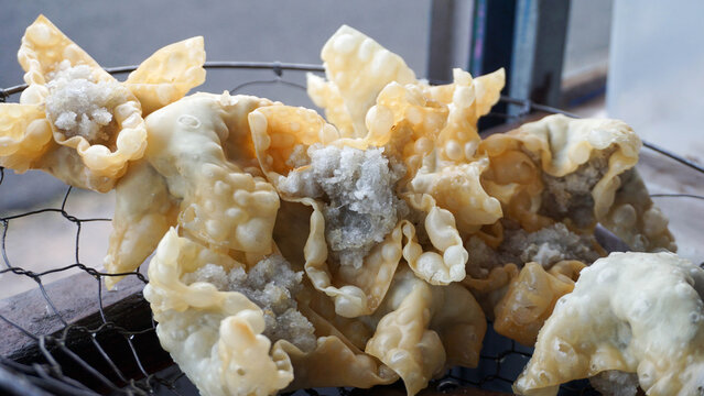 Detailed close up shot of golden crispy fried batagor dumplings placed on a metal mesh skimmer after deep frying.