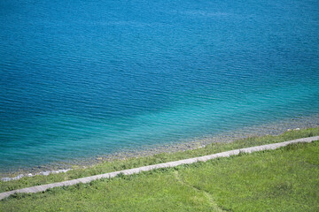 Obraz premium Aerial View of Sayram Lake Shoreline Tourists Walking on Wooden Boardwalk, Green Grassland and Azure Water in Xinjiang