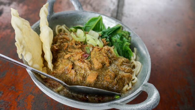 Close up view of Indonesian chicken noodle mie ayam loaded with rich savory minced chicken, green mustard, scallions, and crackers in a mini wok bowl.
