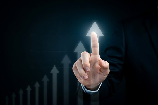 Businessman's finger touches an upward arrow, representing financial growth and market success.