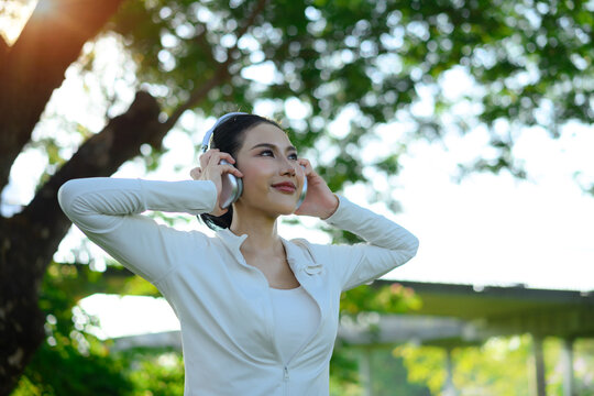 Woman enjoying music with headphones in park, uplifting wellness moment.