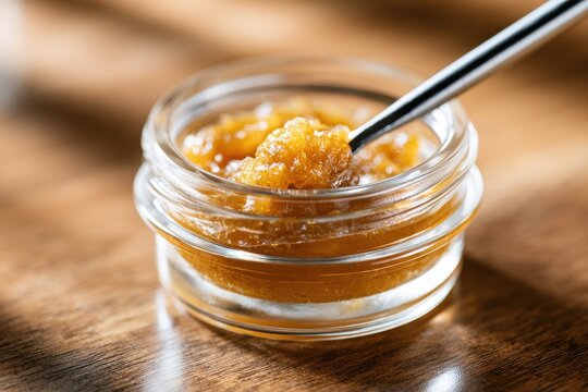 Glossy cannabis extract in a small container with a precision dab tool, warm tones