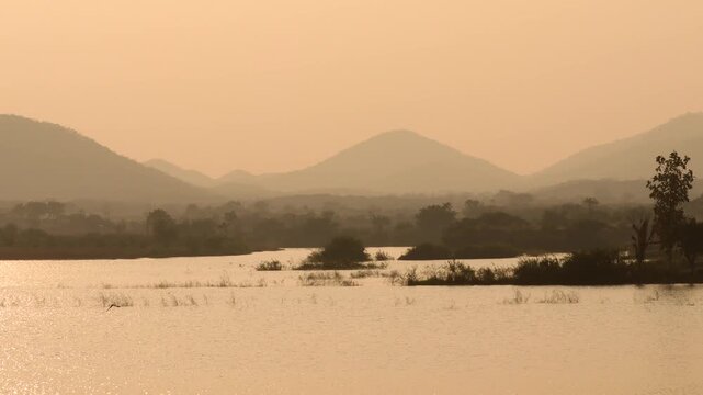 Serene Mountain Lake Landscape at Golden HourTranquil Lake and Hills in Warm Evening LightPeaceful Misty Mountain Waterfront Silhouette at Sunset.
