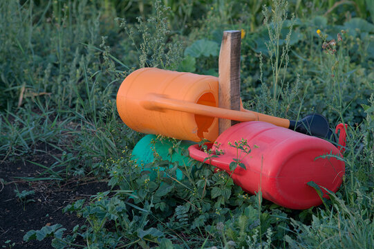 Symbol of climate change. Three colorful watering cans rest unused on a wooden pole. A powerful metaphor for summer drought, water scarcity, heatwaves, and challenges in modern agriculture.
